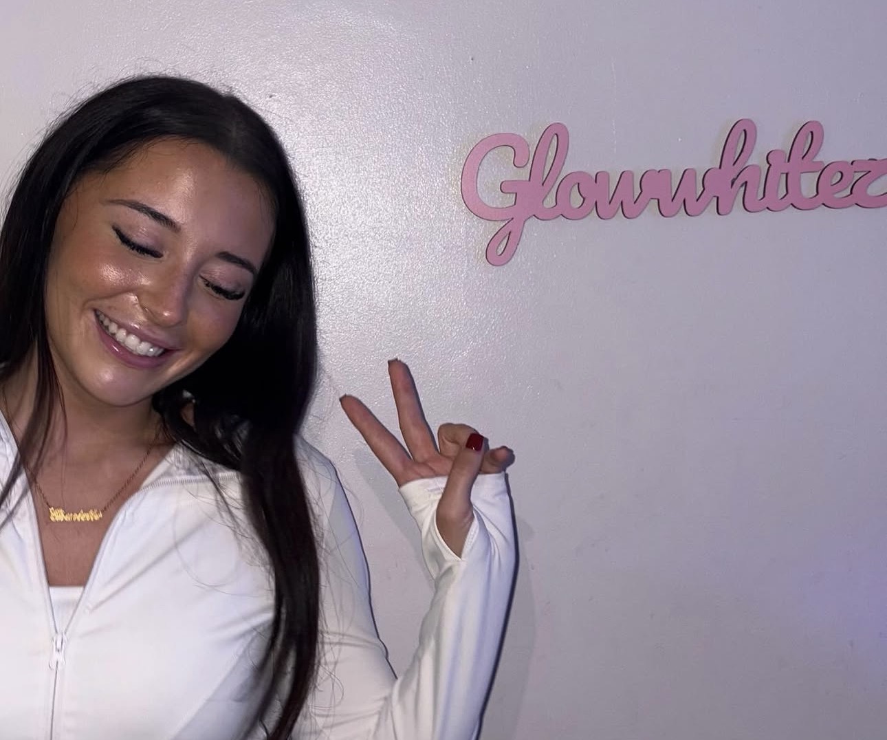 A client smiling beside the Glow Whitez signage
